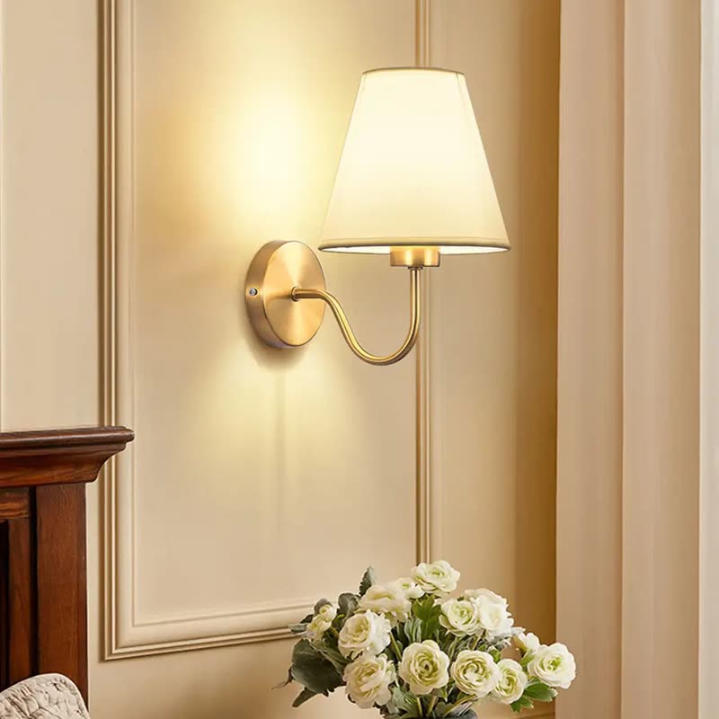 Brass wall sconce with a curved arm and a white fabric shade, lit on a cream wall (seller photo from the AliExpress listing)
