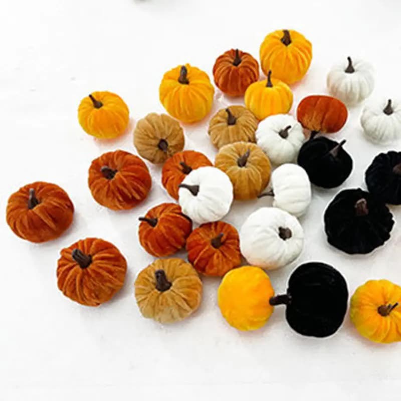 Mini velvet-look pumpkins in orange, mustard, cream and black scattered on a white surface (seller photo from the AliExpress listing)