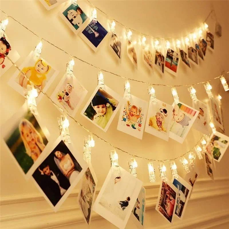 Photos clipped along strands of warm LED fairy lights hanging on a wall (seller photo from the AliExpress listing)