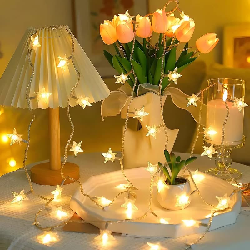 Warm star-shaped string lights draped around a table lamp, a vase of tulips and candles (seller photo from the AliExpress listing)